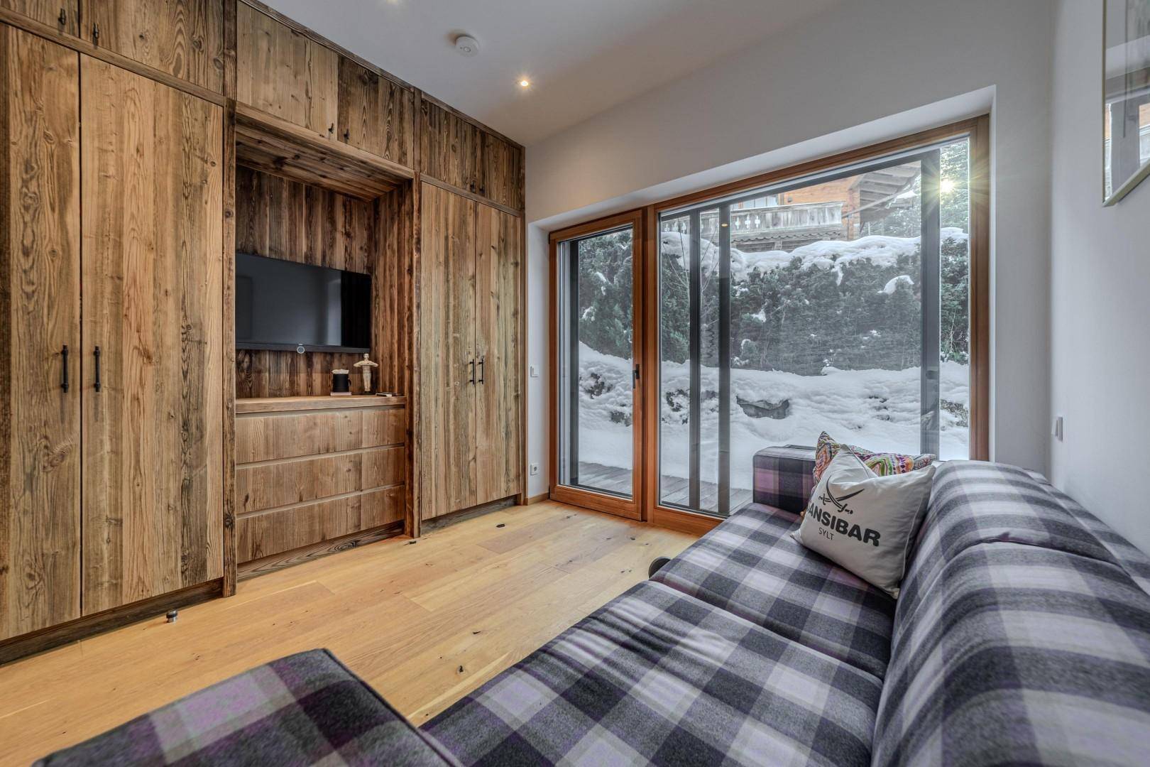 Gemütliches Schlafzimmer mit kariertem Sofa, Holzeinbauschränken und Blick ins Grüne.