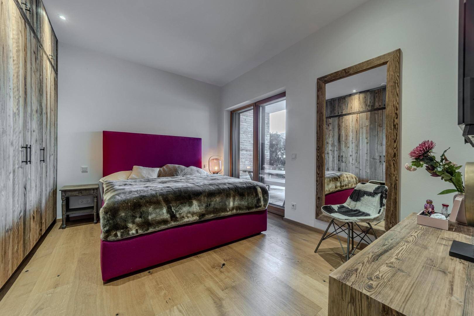 Helles Schlafzimmer mit Holzboden, großem Spiegel und Zugang zum Außenbereich.