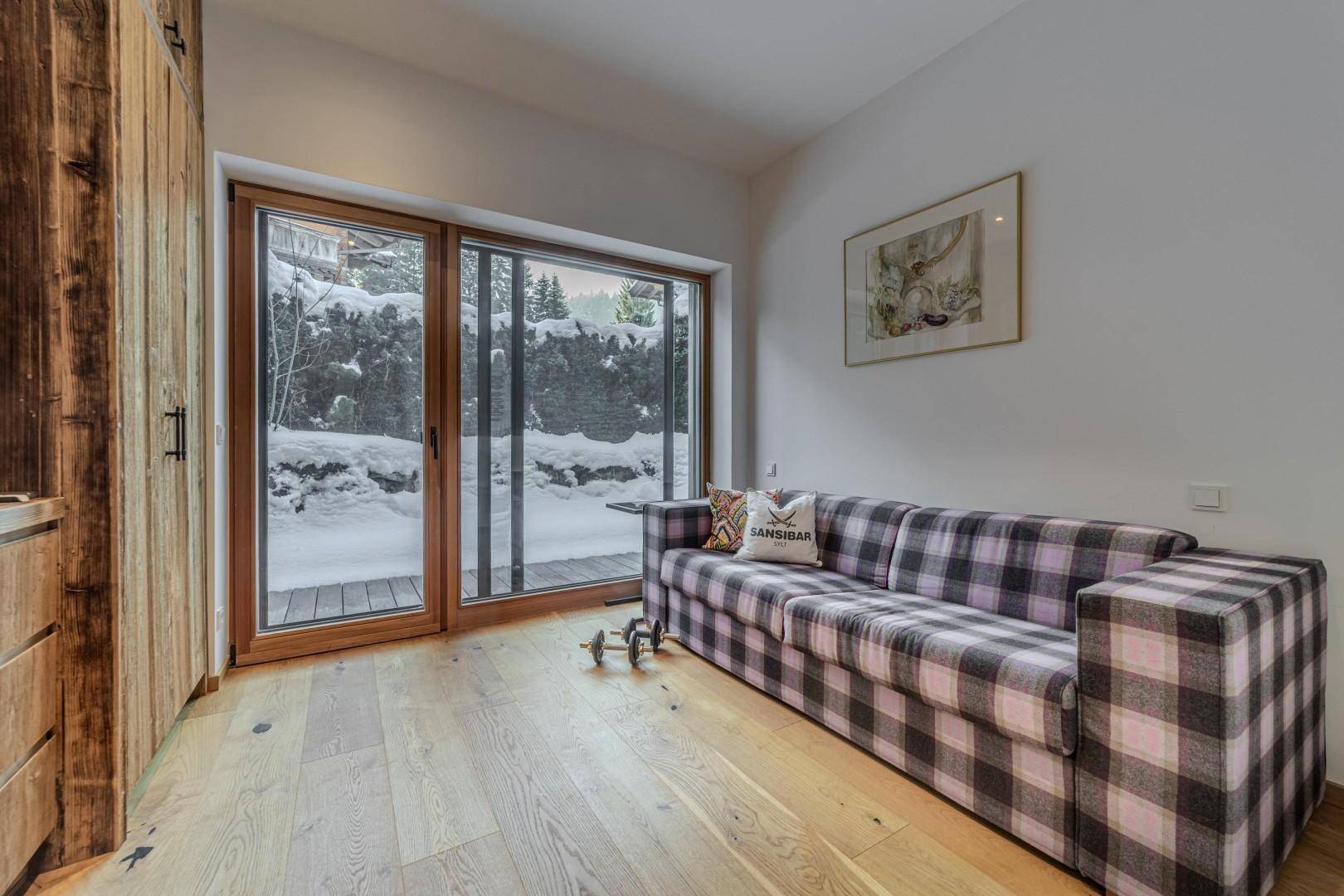 Helles Schlafzimmer mit kariertem Sofa und großem Fenster mit Blick auf die verschneite Umgebung.