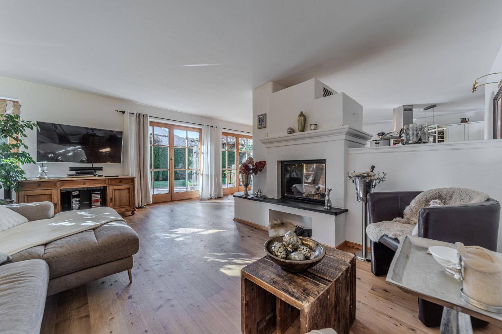 Helles Wohnzimmer mit Kamin, Holzboden und Zugang zur Terrasse durch große Glastüren.