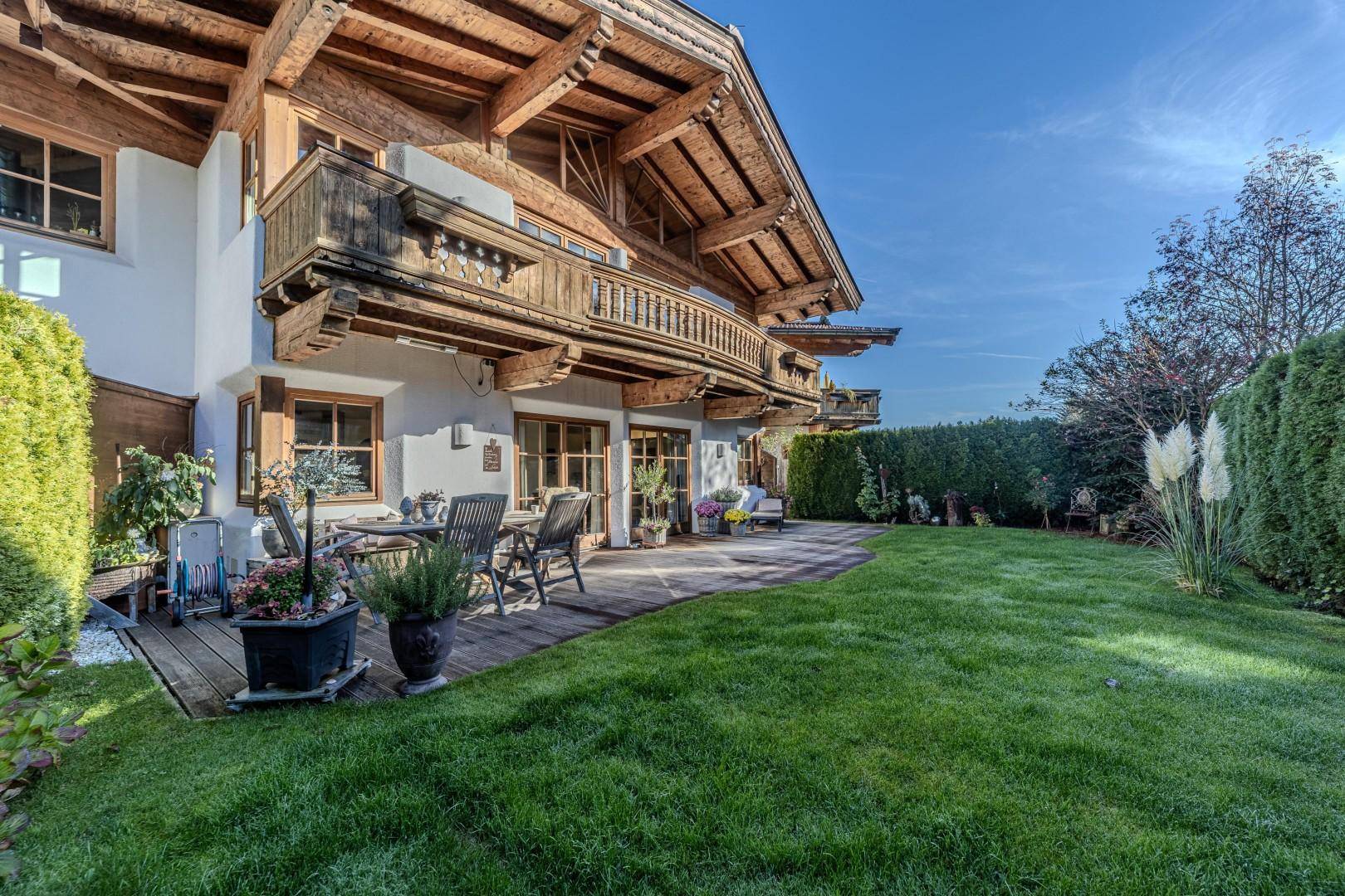 Seitliche Ansicht des Chalets mit sonniger Holzterrasse, umgeben von einem grünen Garten und Hecken.
