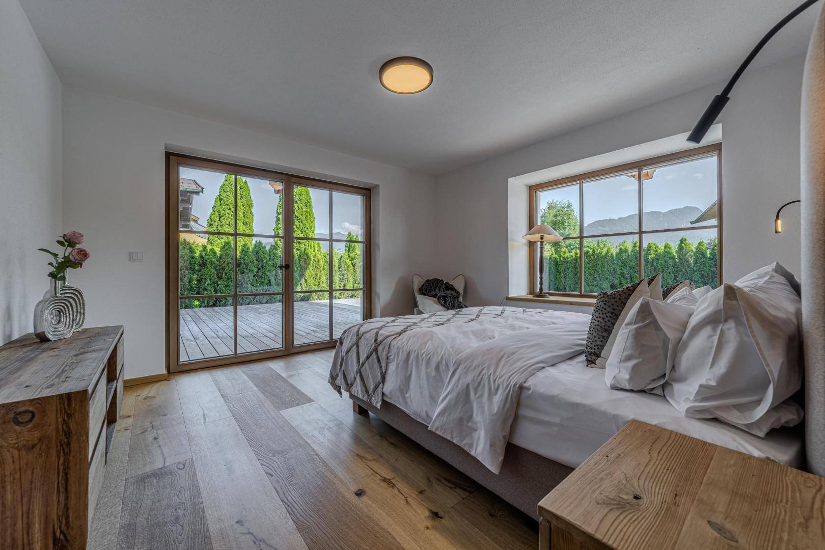 Helles Schlafzimmer mit Holzboden, großen Fenstern und Zugang zum Außenbereich.