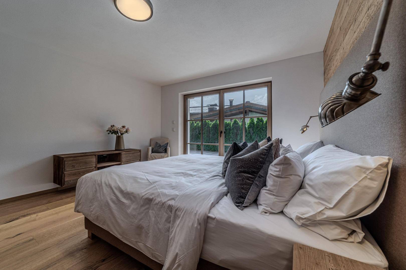 Gemütliches Schlafzimmer mit Holzboden, großen Fenstern und Blick auf die Umgebung.