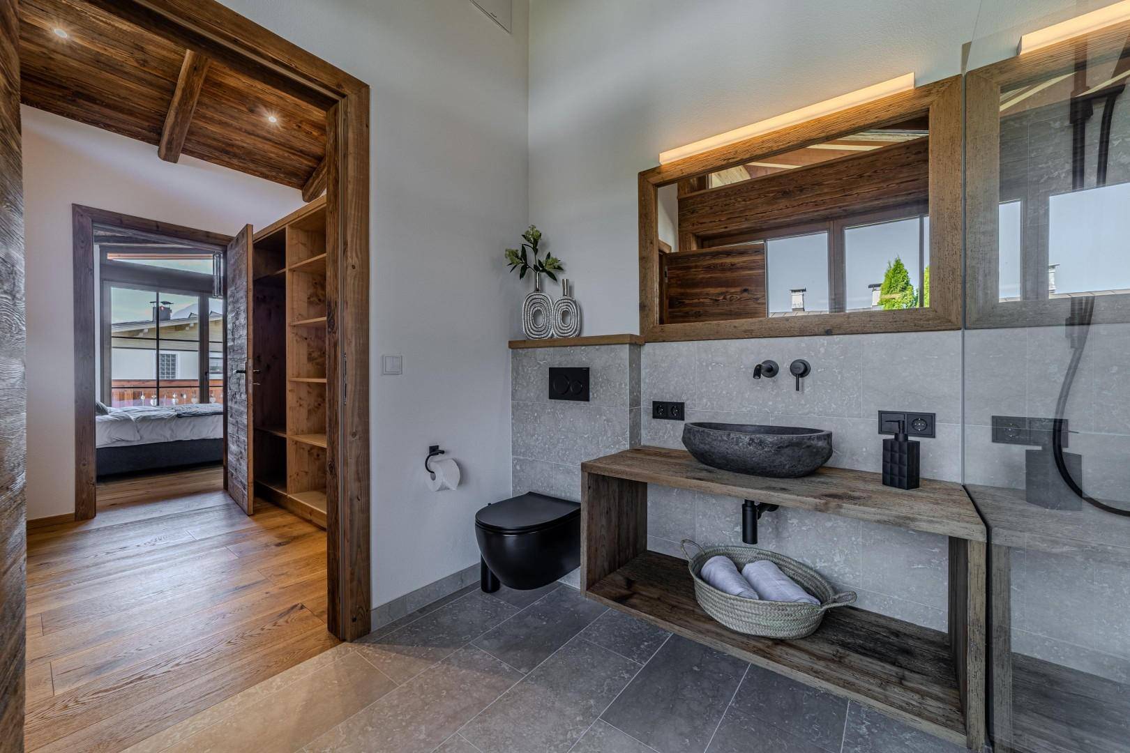 Modernes Badezimmer mit Steinwaschbecken, begehbarer Dusche und Zugang zum Schlafzimmer.