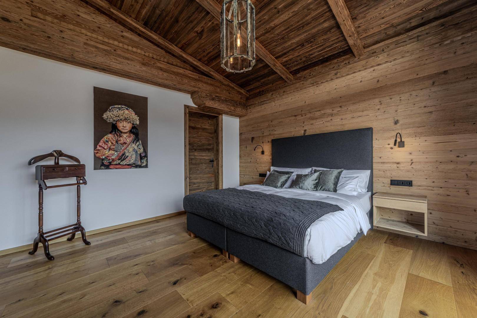 Gemütliches Schlafzimmer mit Holzwänden, Holzbalkendecke und modernem Bett.