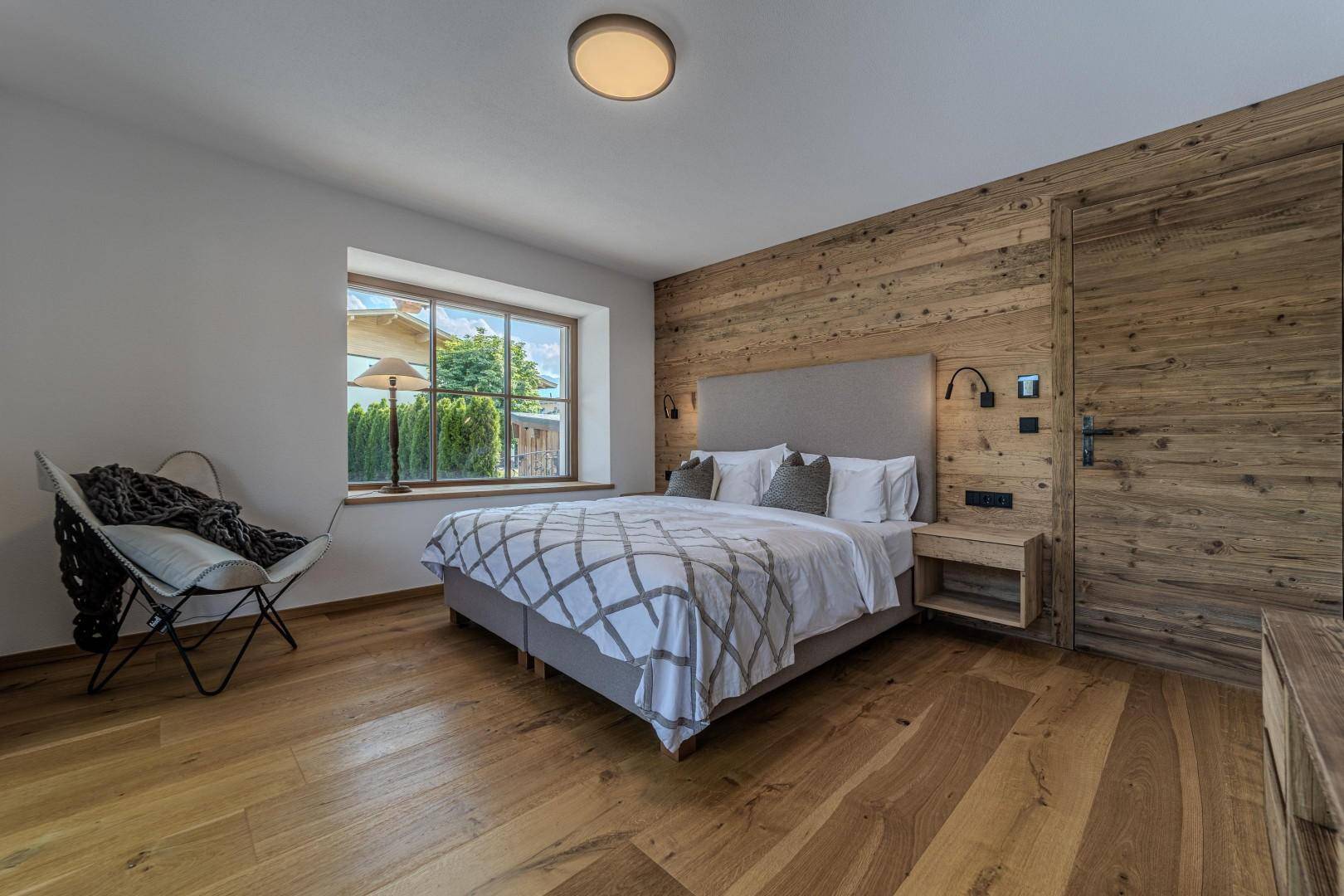 Schlafzimmer mit Holzboden, großen Fenstern und Blick auf die grüne Umgebung.