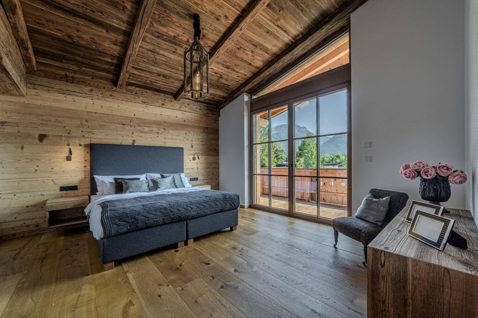 Schlafzimmer im alpinen Stil mit Holzwänden, Holzbalkendecke und Balkonzugang mit Bergblick.