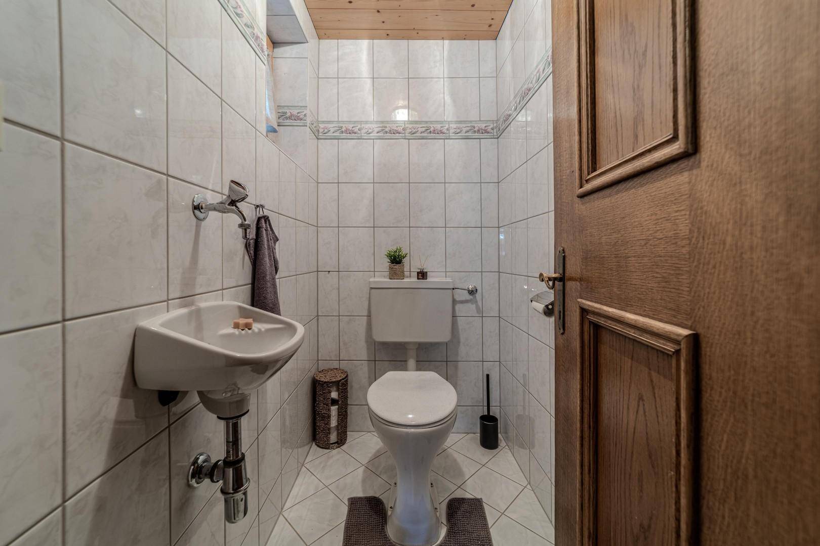 Separates WC mit Waschbecken, Toilette und hellen Fliesen an den Wänden.
