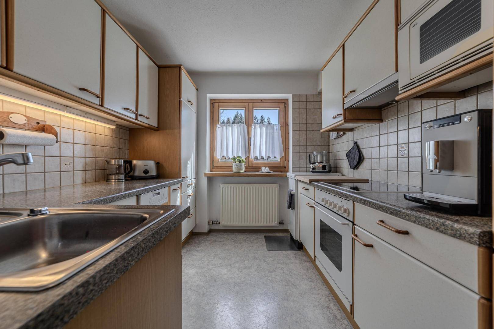 Funktionale Küche mit hellen Schränken, Fliesenboden und Fenster mit Blick nach draußen.