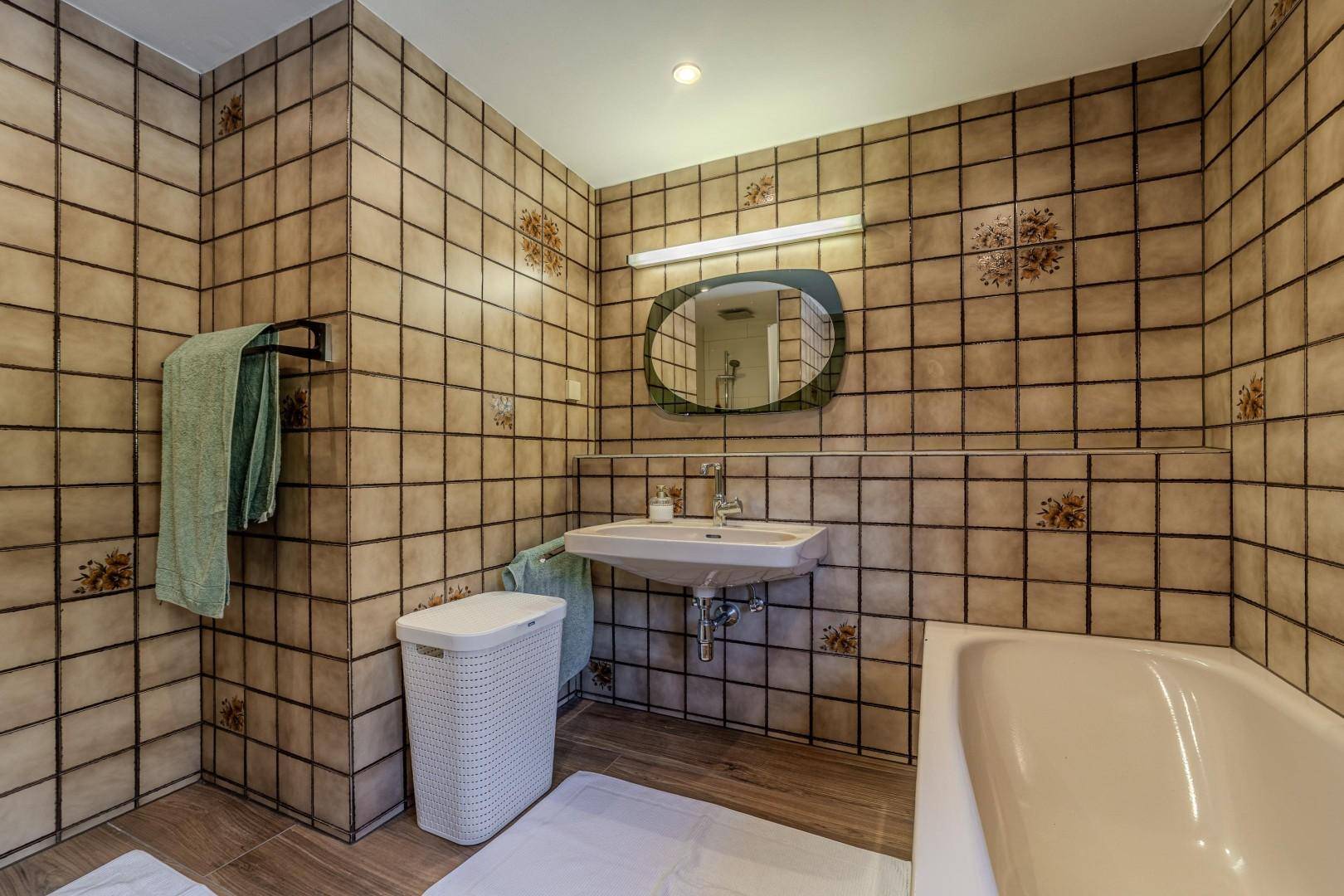 Badezimmer mit Badewanne, Waschbecken und Fliesen an Wänden und Boden.