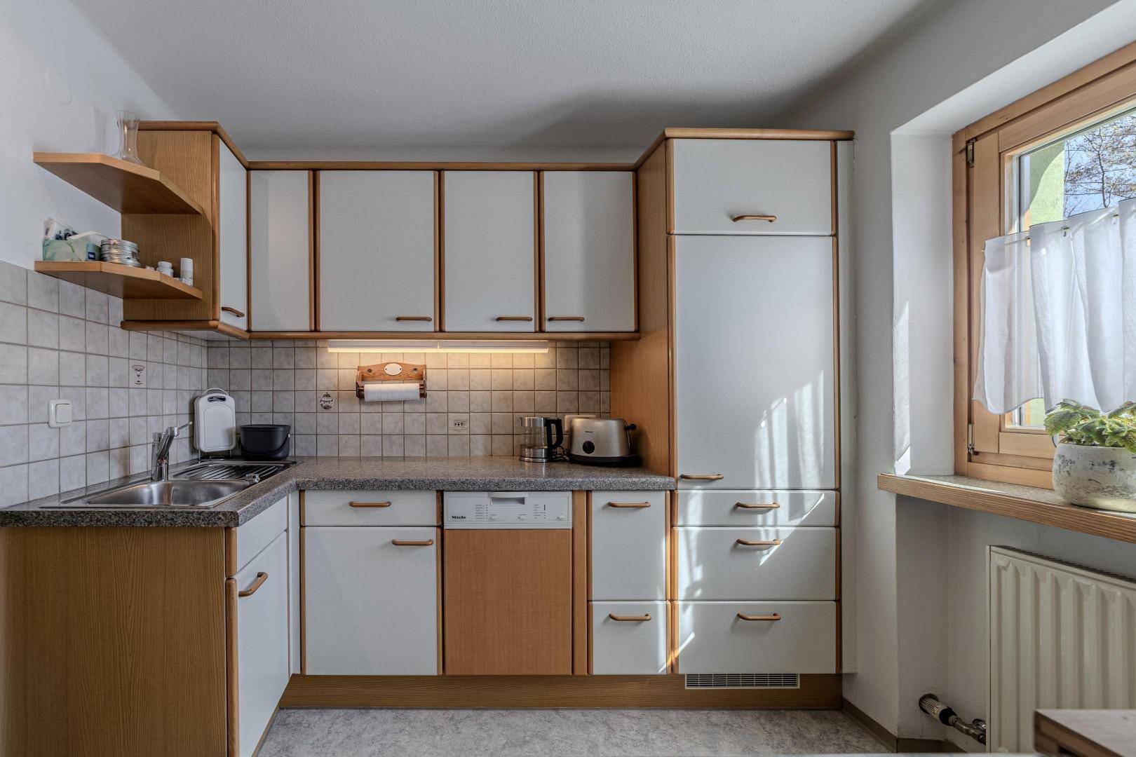 Helle Küche mit weiß-holzfarbenen Schränken, Fliesenrückwand und großem Fenster.
