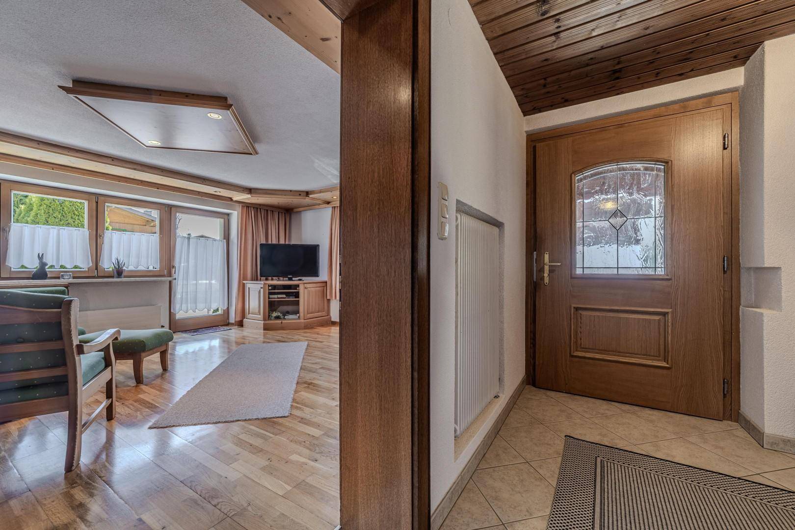 Gemütlicher Eingangsbereich mit Holztür und Fliesenboden, der in ein helles Wohnzimmer mit Holzboden führt.