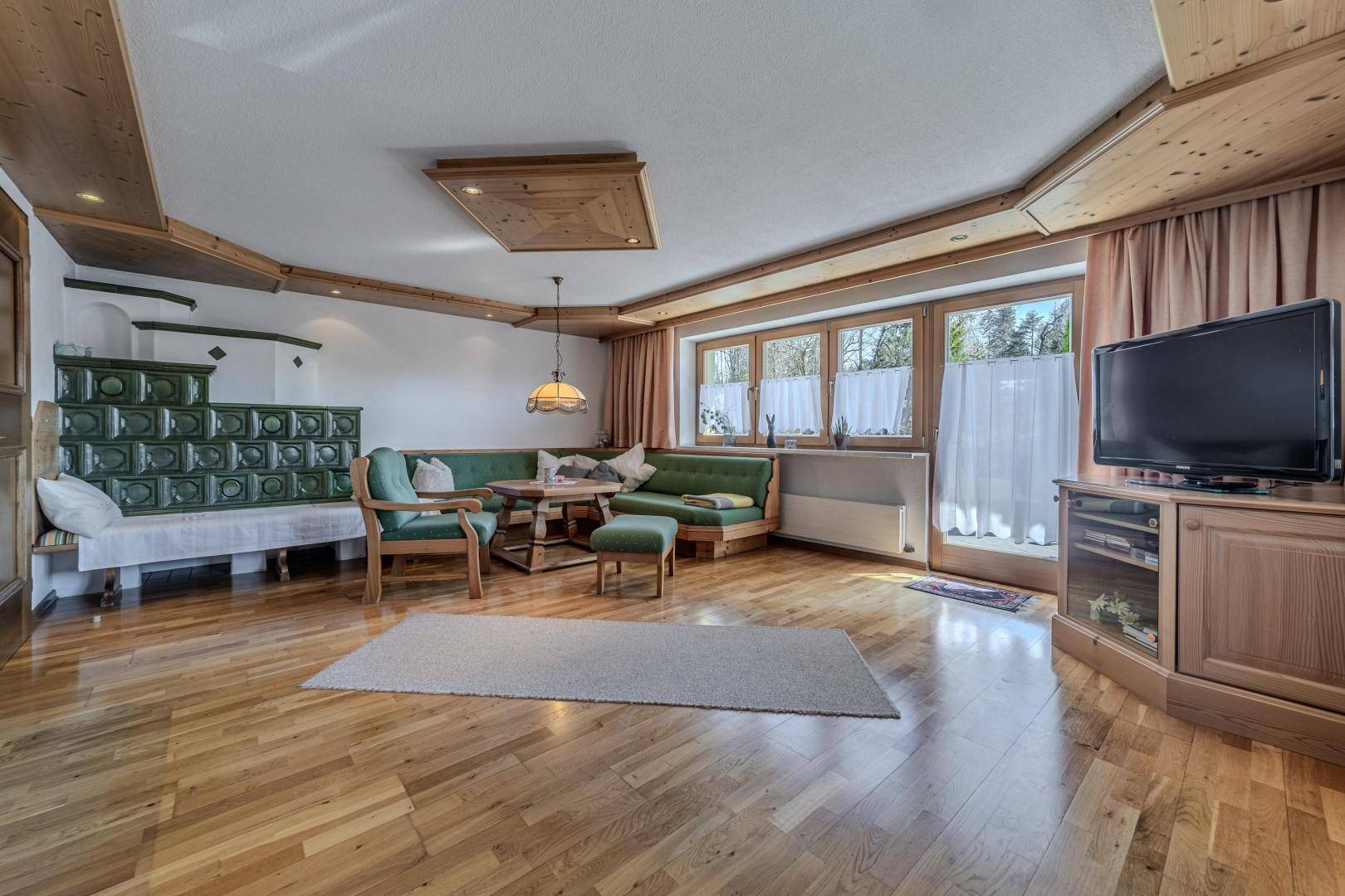 Gemütliches Wohnzimmer im alpinen Stil mit Kachelofen, Holzboden und traditionellen Möbeln.