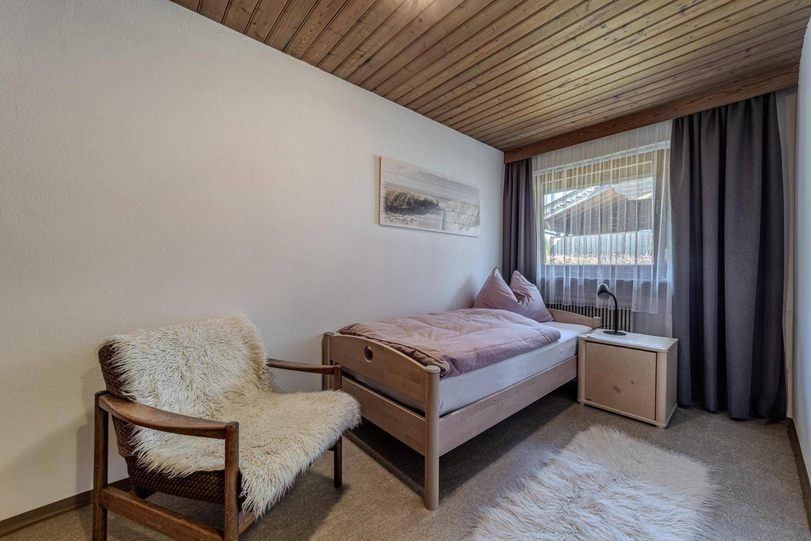 Helles Schlafzimmer mit Einzelbett, Holzdecke und Teppichboden, ideal als Gästezimmer.