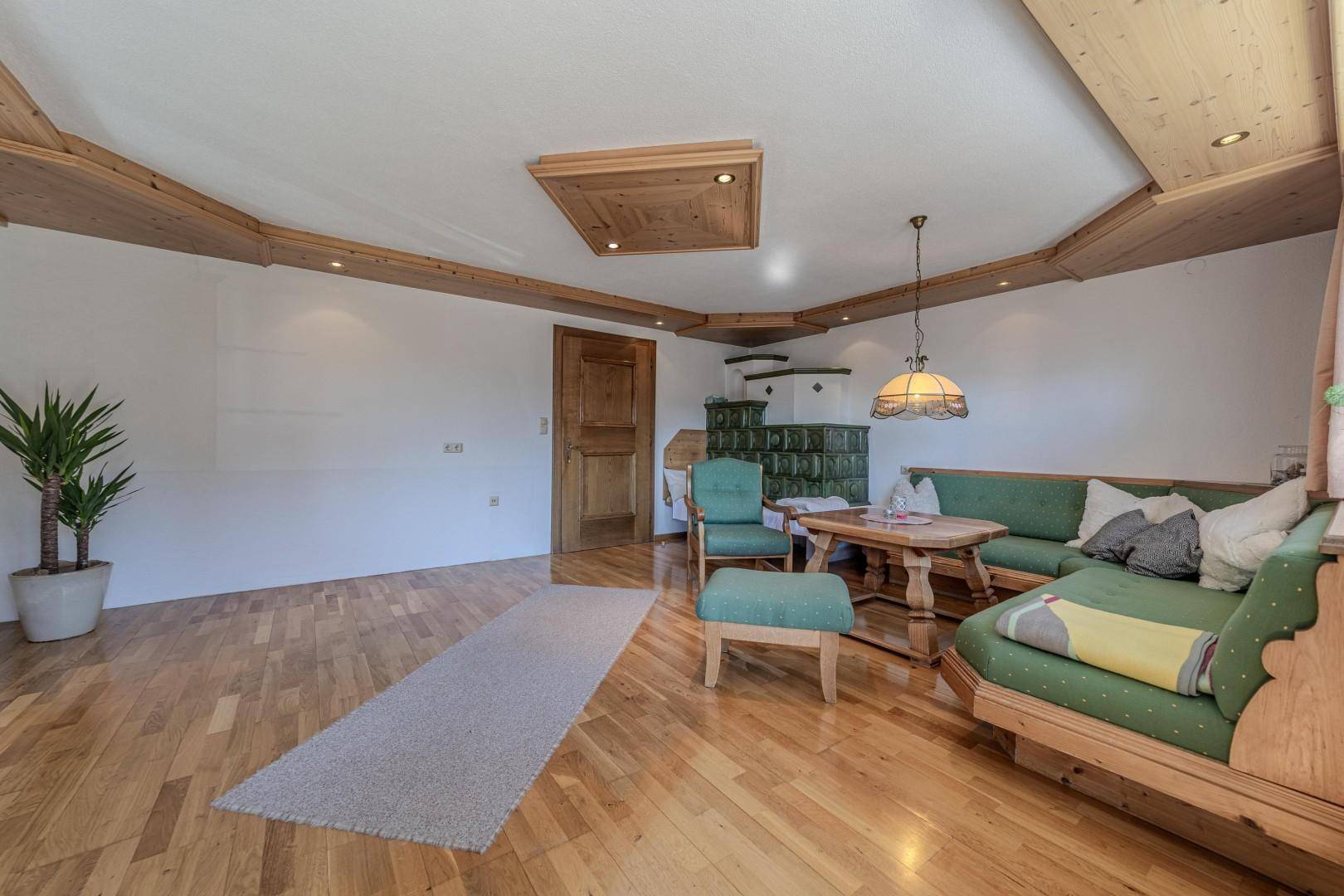 Geräumiges Wohnzimmer mit Holzboden, Kachelofen und viel Platz für geselliges Beisammensein.