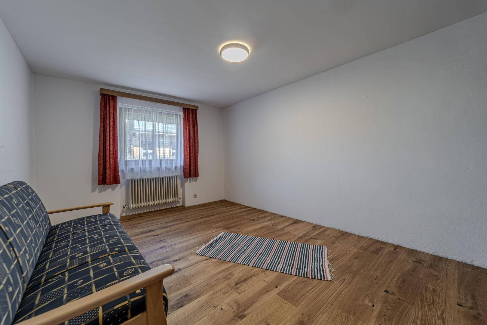 Geräumiges Zimmer mit Holzboden, Fenster und einfacher Einrichtung, vielseitig nutzbar.