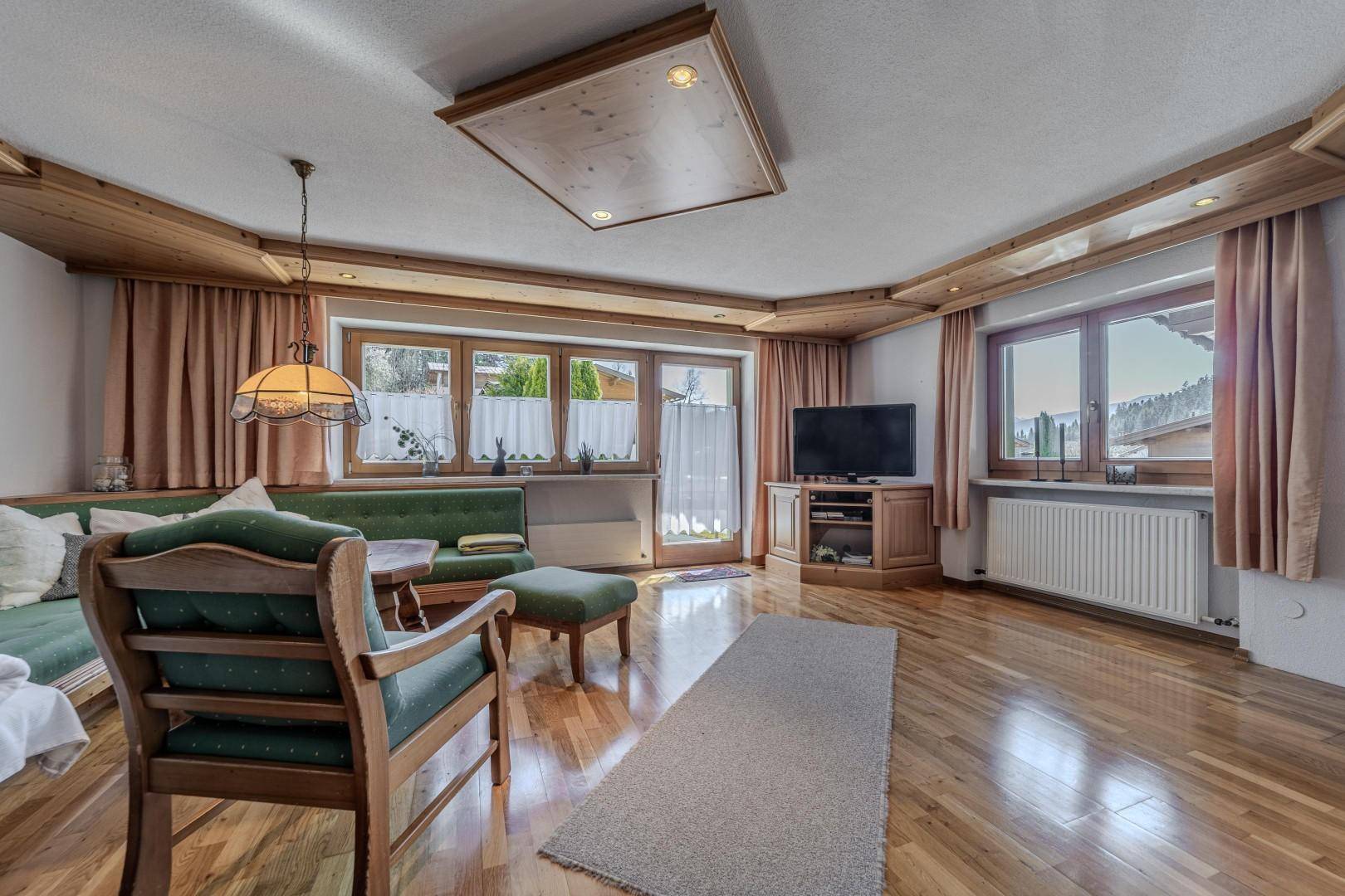 Wohnzimmer mit Fernseher, Holzboden und Zugang zu einem Außenbereich durch eine Glastür.