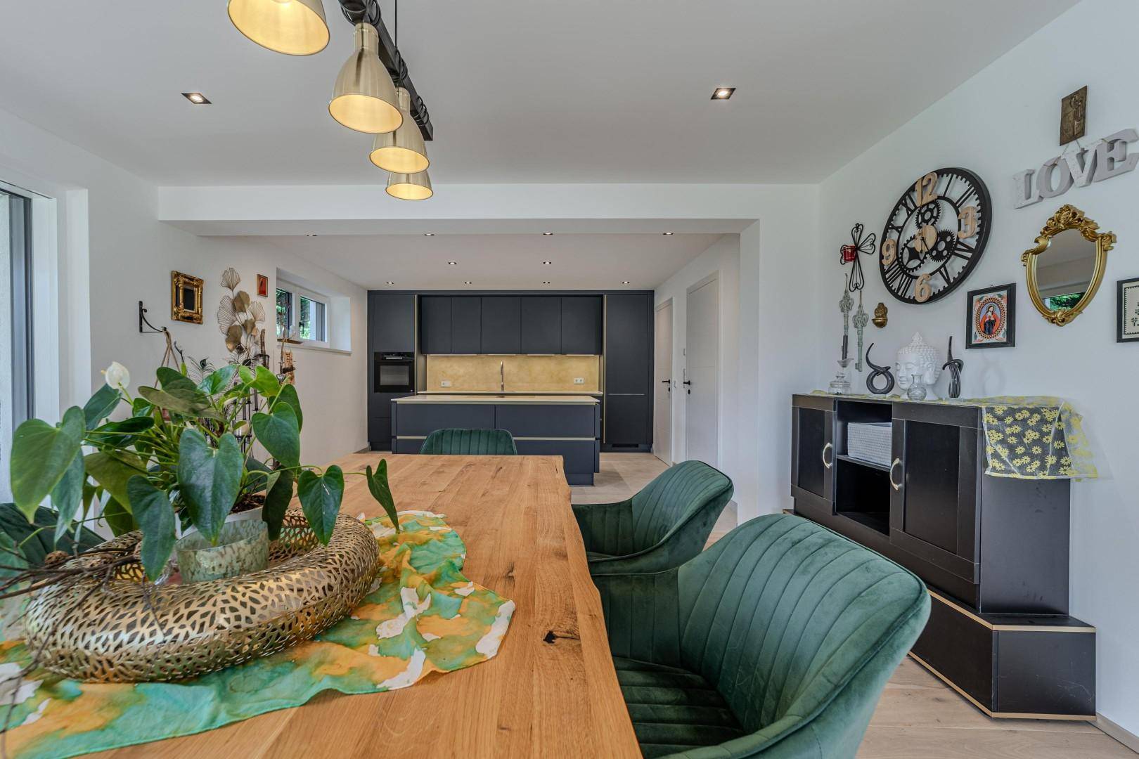 Detailansicht des Essbereichs mit Holztisch und grünen Stühlen, die moderne Küche ist im Hintergrund sichtbar.