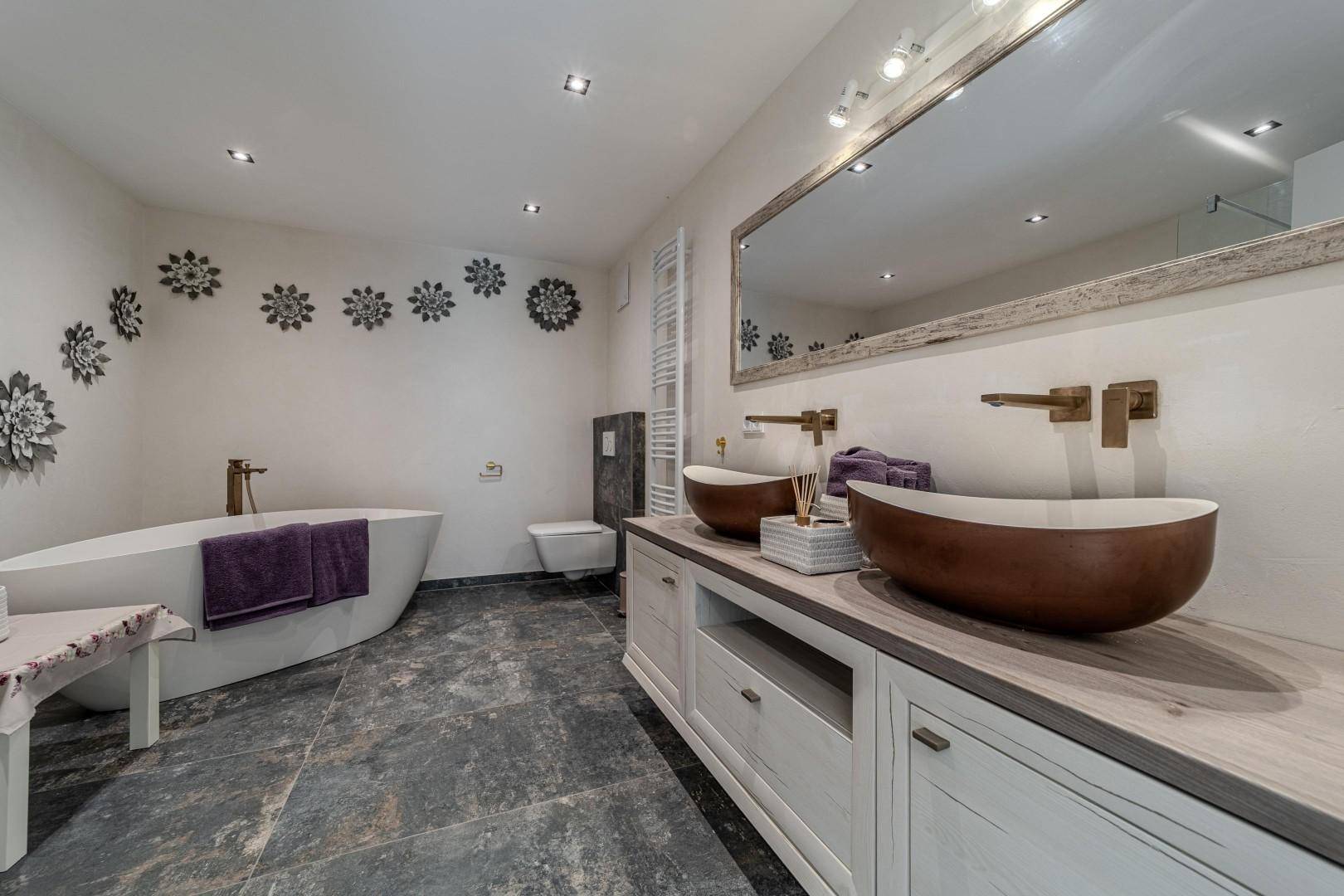 Modernes Badezimmer mit freistehender Badewanne, Doppelwaschbecken und dunklen Fliesen.