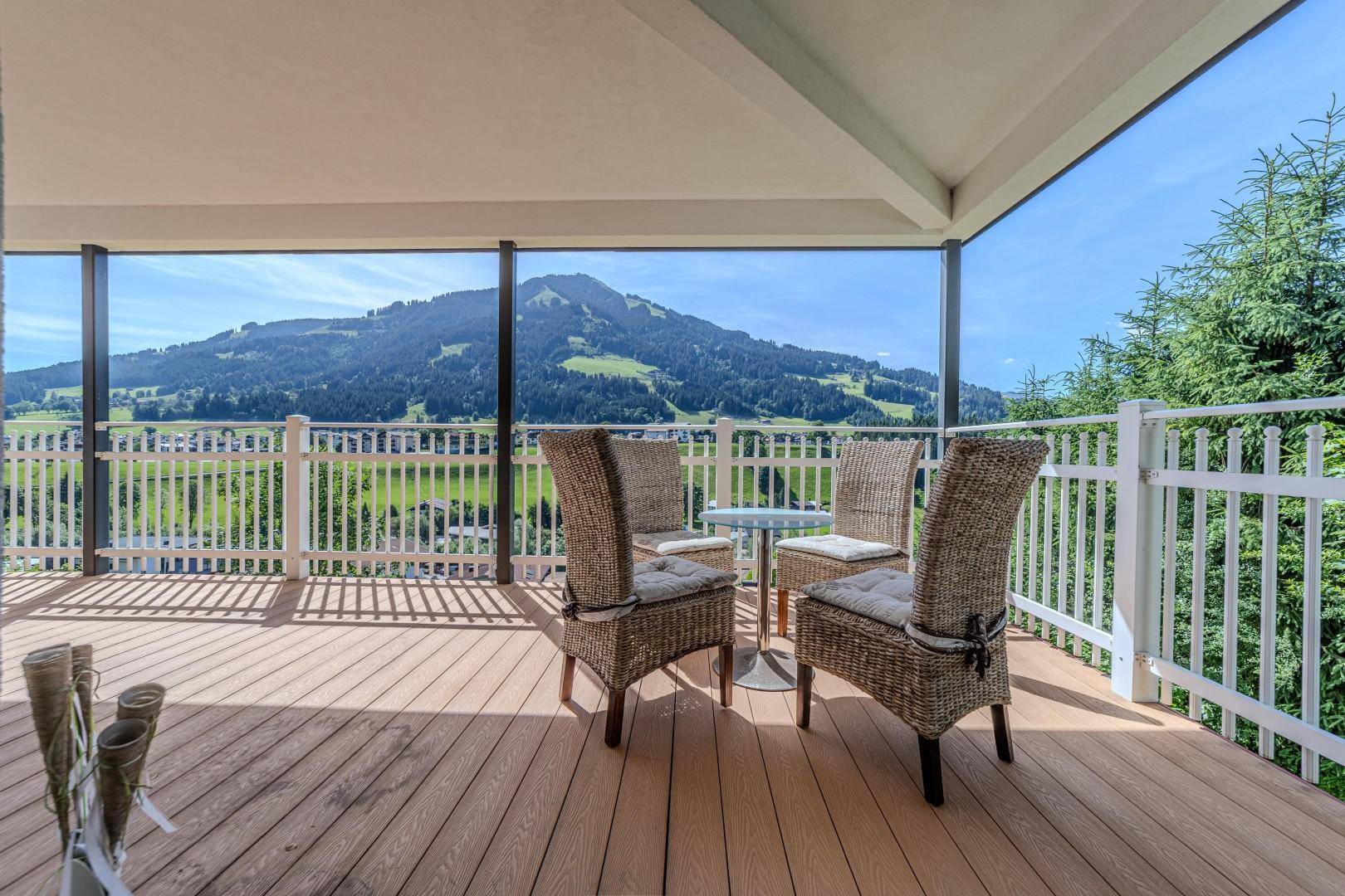 Überdachter Balkon mit Rattanmöbeln und direktem Blick auf die majestätische grüne Bergkulisse.