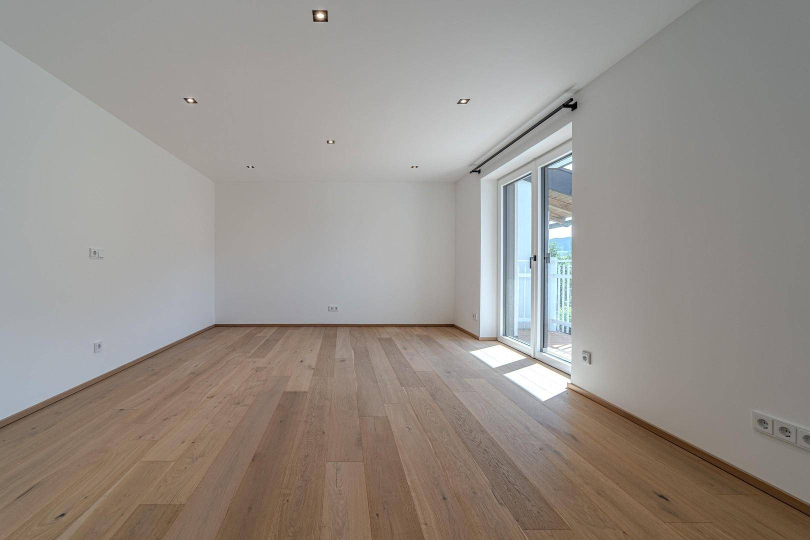 Heller, leerer Raum mit hellem Holzboden und Zugang zu einem Balkon mit Bergblick.