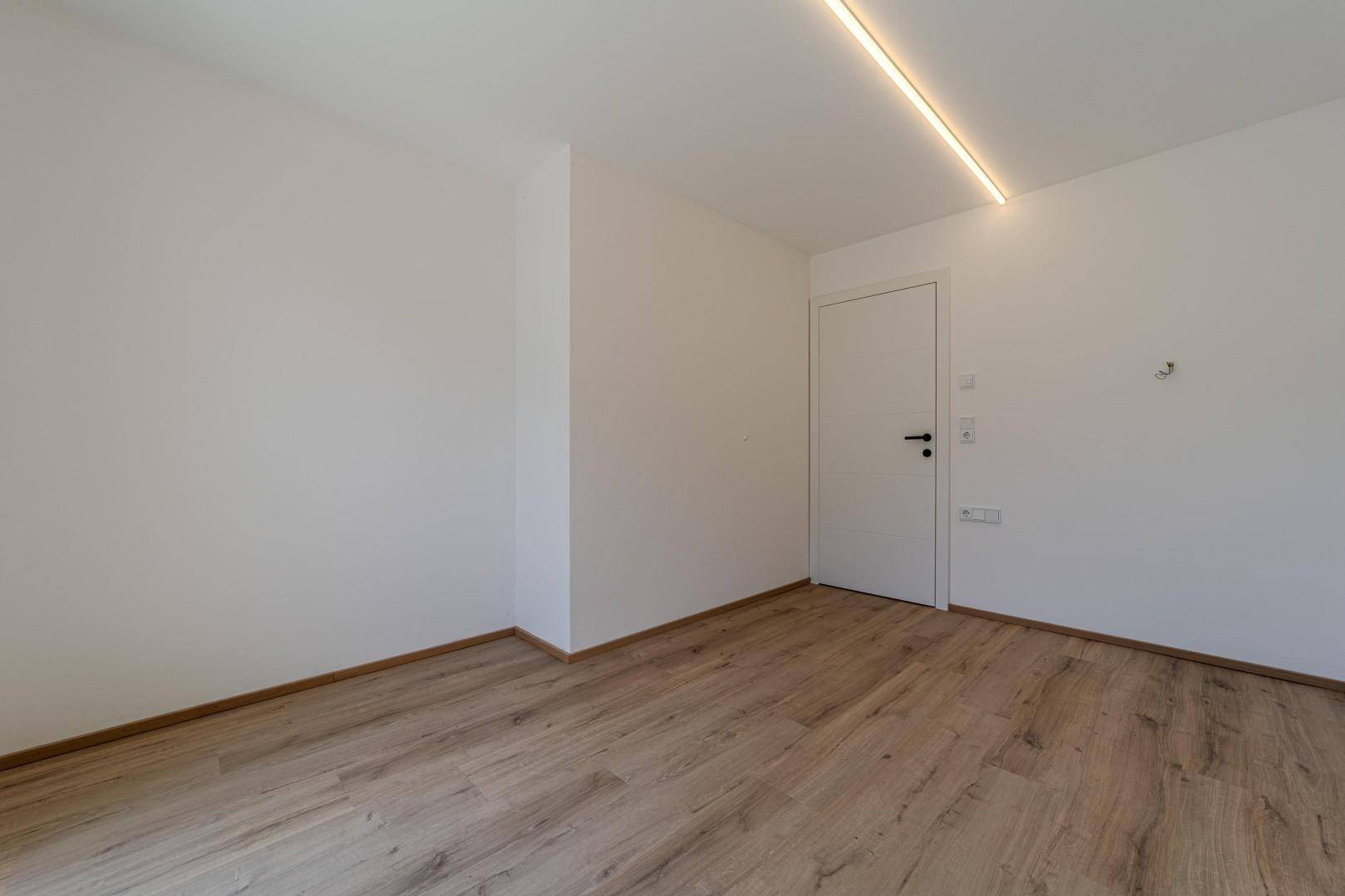 Leerer Raum mit hellem Holzboden und weißen Wänden, ideal als Schlaf- oder Arbeitszimmer.
