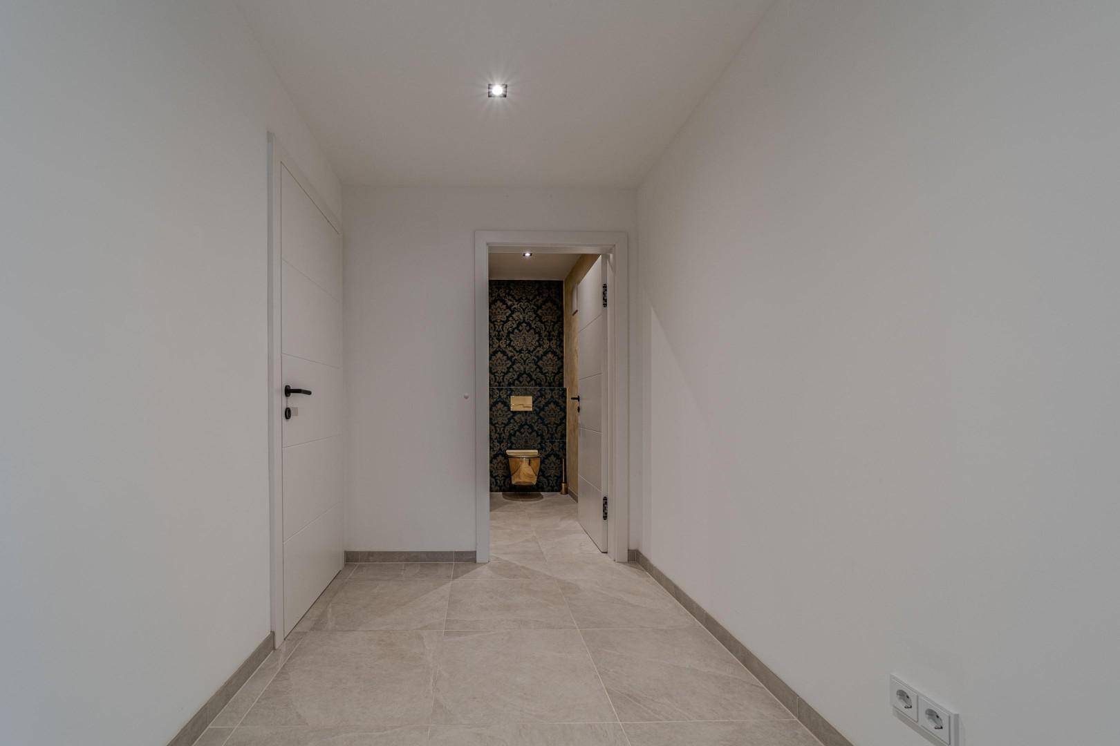 Heller Flur mit Fliesenboden und weiß gestrichenen Wänden, führt zu einem Badezimmer.