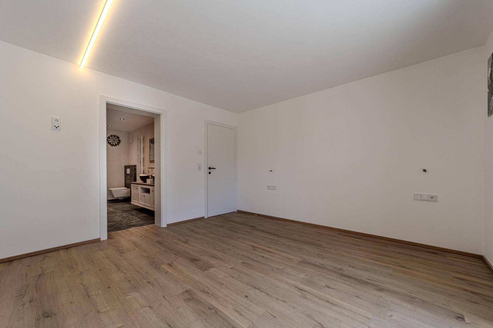 Unmöblierter Raum mit Holzboden und Zugang zu einem modernen Badezimmer.