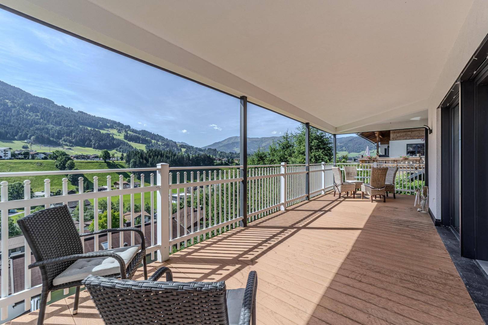 Langer überdachter Balkon mit weißem Geländer und atemberaubendem Panoramablick auf die Berge.