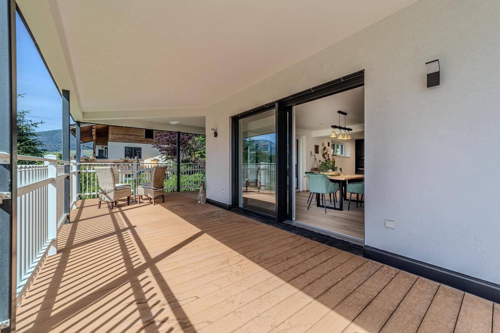 Überdachter Balkon mit Holzdeck und Schiebetüren, die zum hellen Essbereich führen.