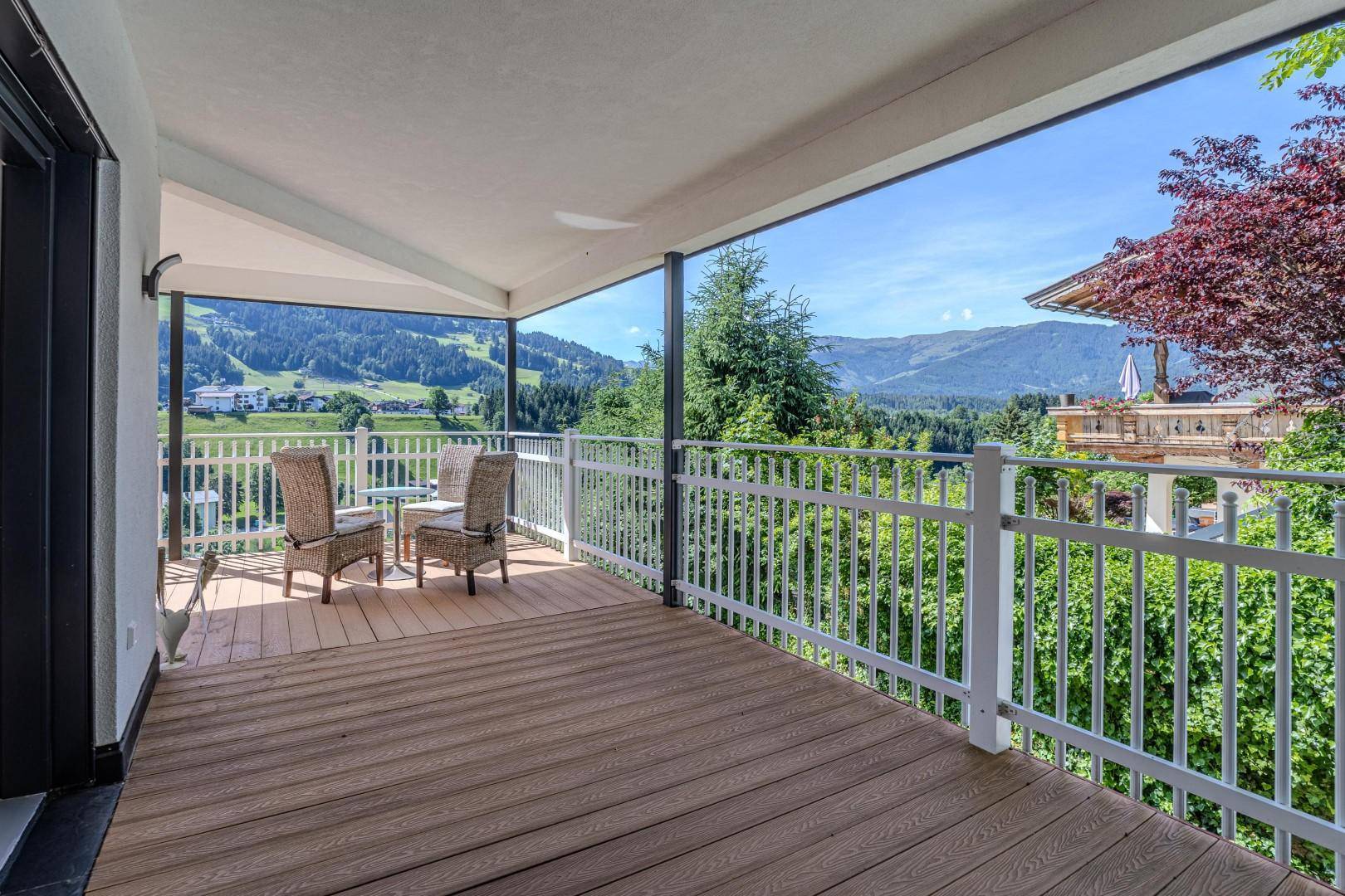 Überdachter Balkon mit Sitzgelegenheiten und weitem Blick über das grüne Tal und die Berge.