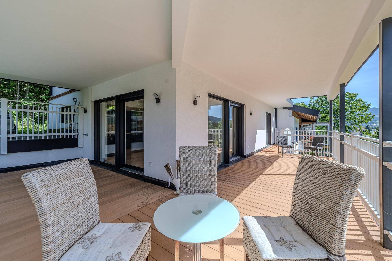 Breiter überdachter Balkon mit Rattanmöbeln und Blick auf die umliegende Landschaft.