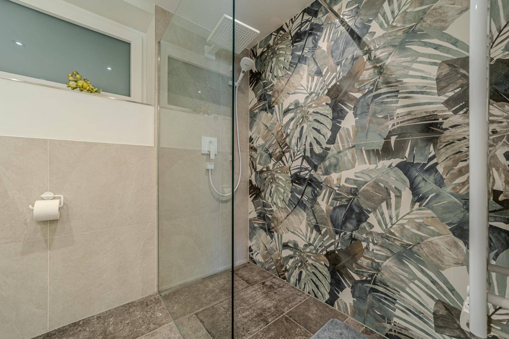 Begehbare Dusche mit auffälliger tropischer Blattmuster-Wand und dunklem Fliesenboden.