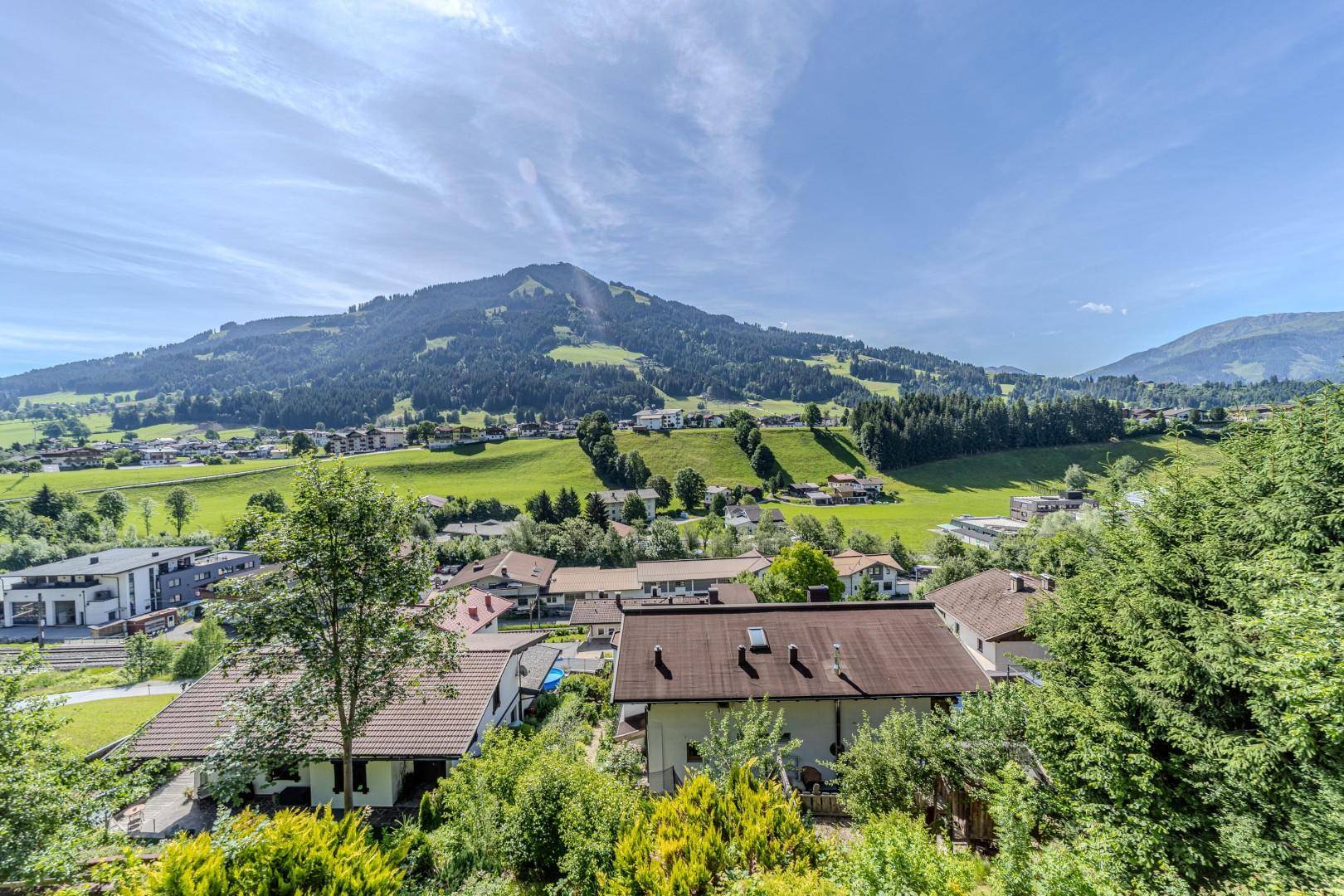 Panoramablick auf ein Dorf im Tal, umgeben von grünen Bergen unter blauem Himmel.