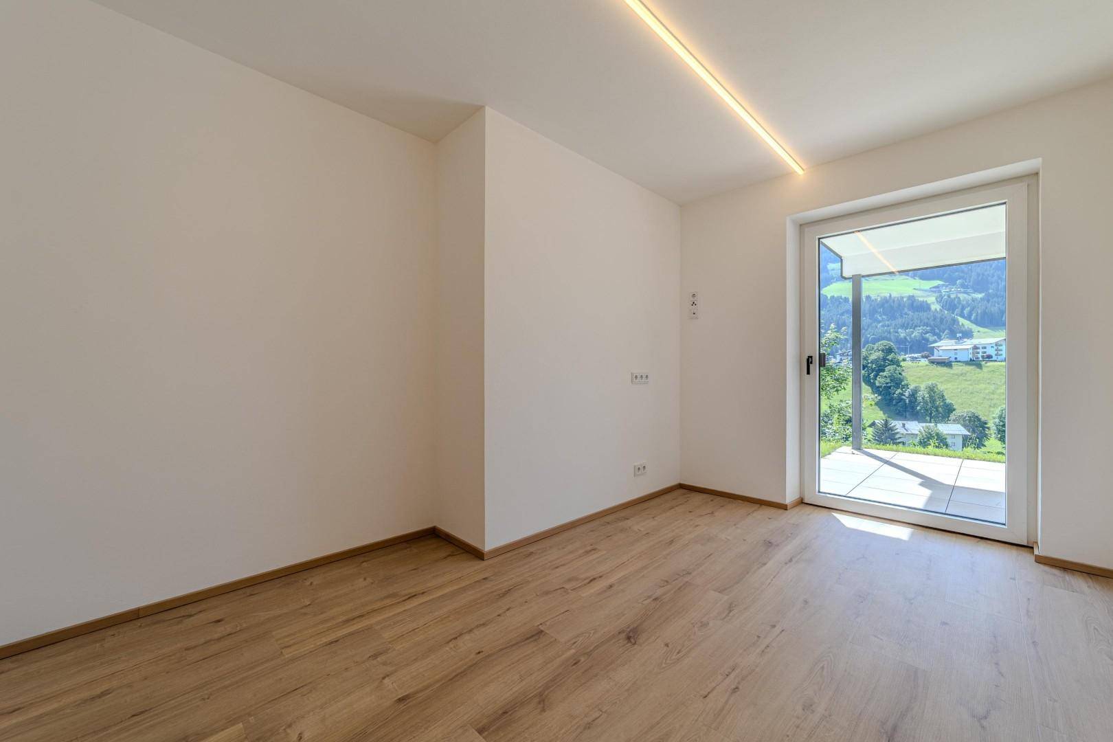 Lichtdurchfluteter Raum mit modernem Holzboden und direktem Zugang zur Außenterrasse mit Alpenblick.