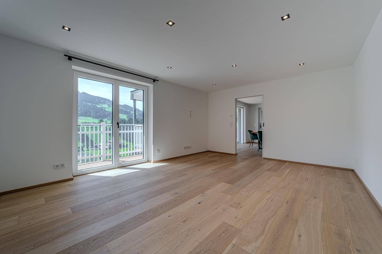 Heller, leerer Raum mit Holzboden und Schiebetür zum Balkon, bietet einen weiten Bergblick.