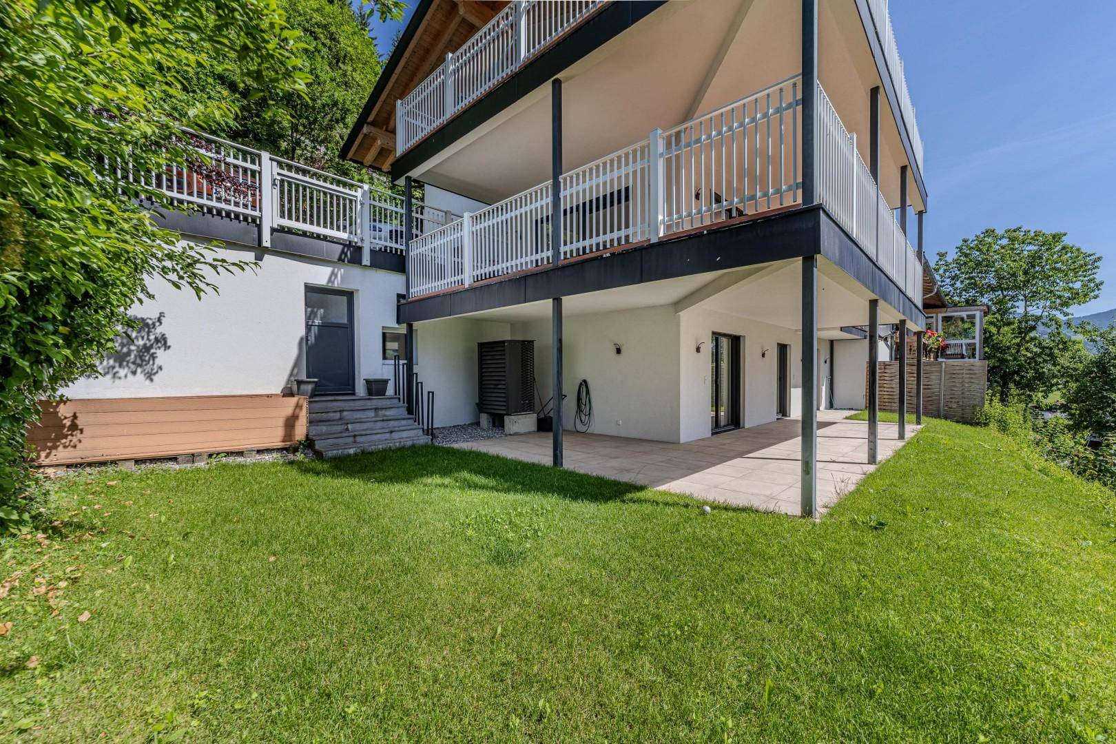 Modernes Gebäude mit mehreren Balkonen und Terrassen, eingebettet in grüne Hügellandschaft.