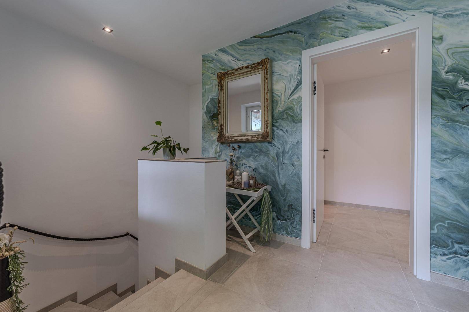 Heller Flur mit Treppenaufgang und einer auffälligen grünen Marmor-Effekt-Wand.