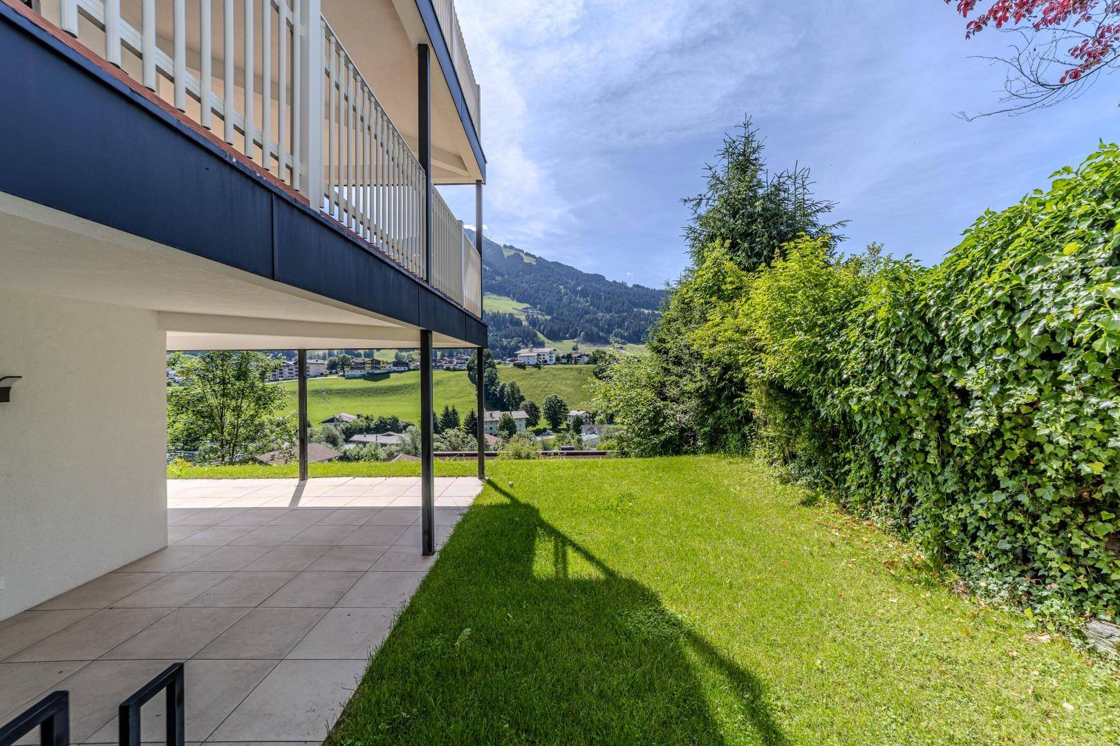 Gartenbereich mit gefliester Terrasse und Rasenfläche, umgeben von üppigem Grün und Bäumen.