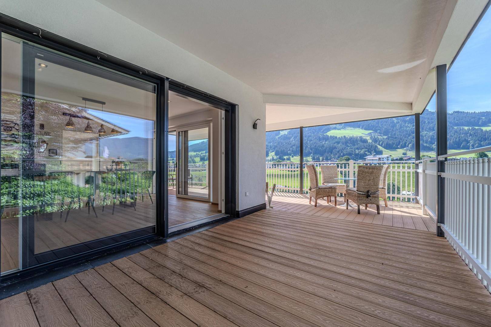 Geräumiger überdachter Balkon mit Holzdeck und Sitzgelegenheiten, bietet einen weiten Blick ins Grüne.