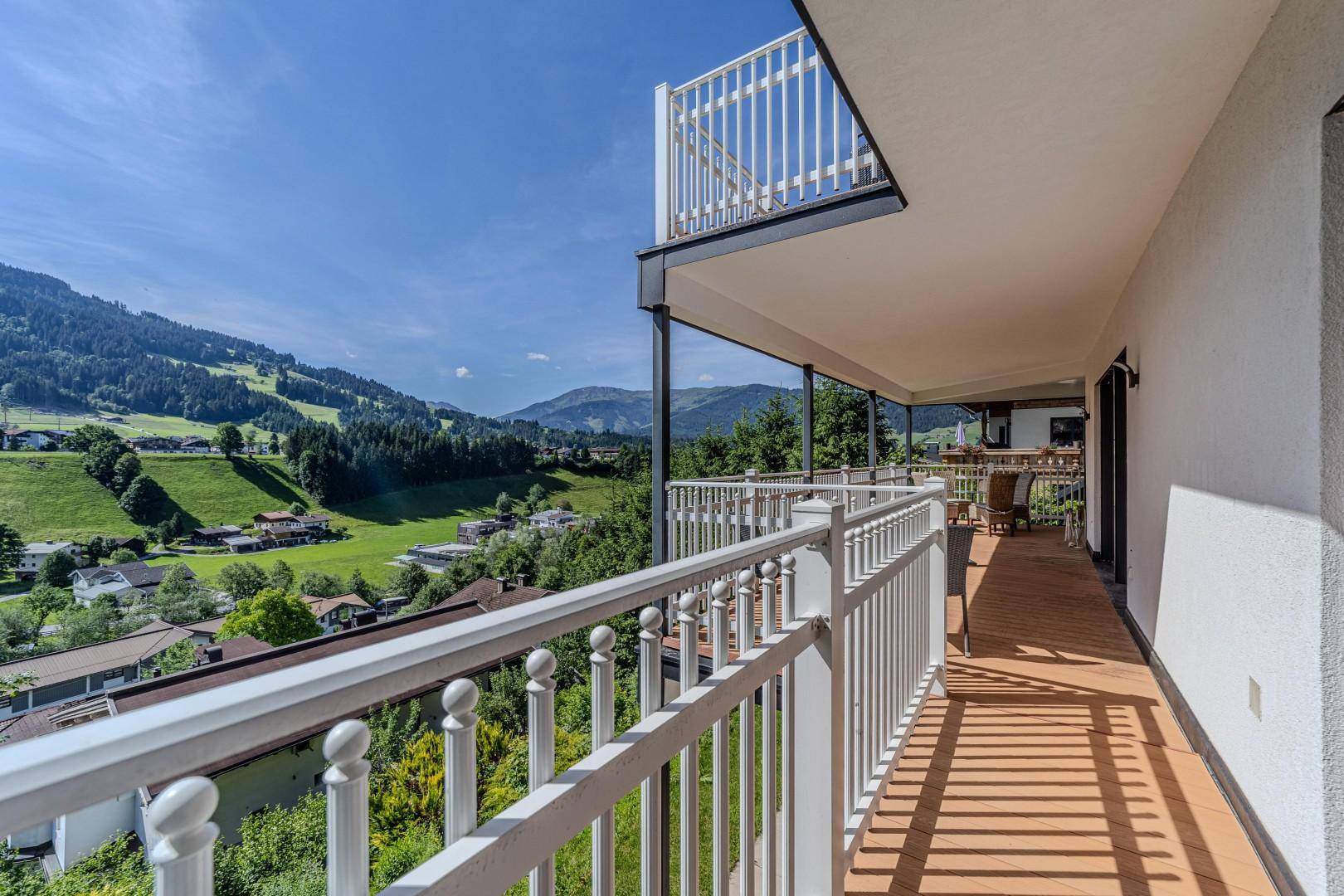 Balkon mit weißem Geländer und freiem Blick auf die grüne Berglandschaft und umliegende Häuser.