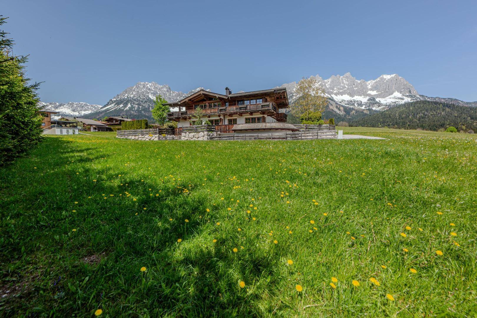 Großes Chalet-Haus in idyllischer Alpenlandschaft mit beeindruckendem Bergblick und weitläufiger Wiese.