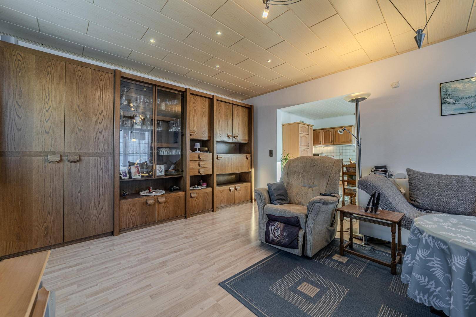 Wohnzimmer mit großer Holzschrankwand, gemütlichem Sessel und Blick in den Essbereich.