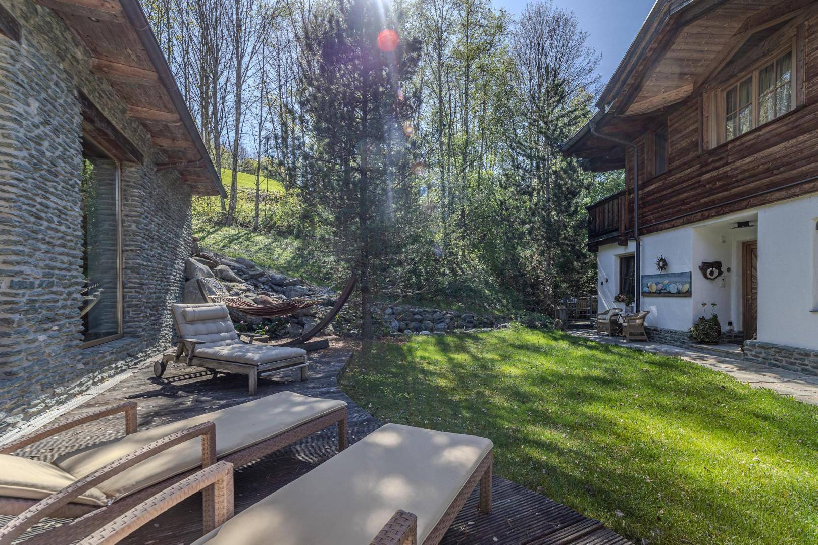 Entspannender Außenbereich mit Holzterrasse, Liegestühlen und Hängematte, umgeben von Natur.