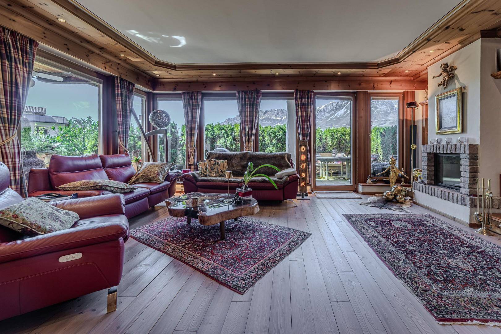 Helles Wohnzimmer mit Holzböden, roten Ledersofas und einem Kamin, umgeben von großen Fenstern.