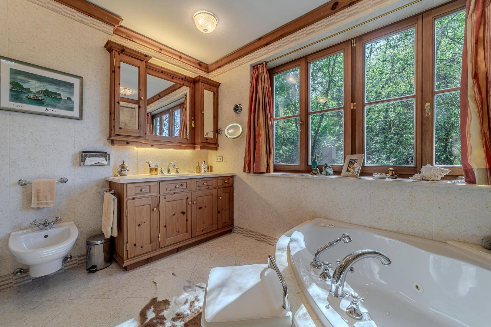 Geräumiges Badezimmer mit Badewanne, Bidet, Doppelwaschbecken und Fenster mit Blick ins Grüne.