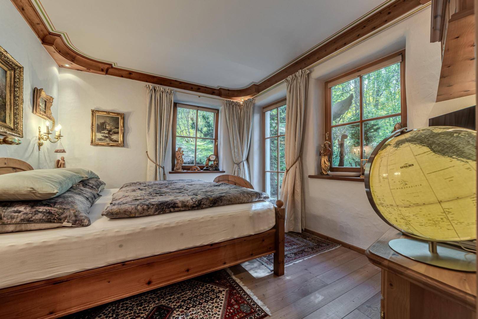 Helles Schlafzimmer mit Holzböden, Doppelbett und großen Fenstern mit Blick ins Grüne.