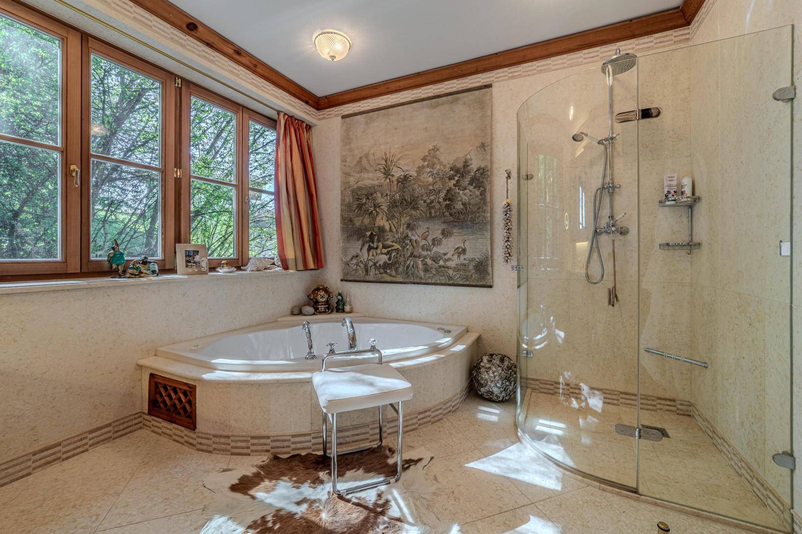 Großes Badezimmer mit Eckbadewanne, Glasdusche und Fenster mit Blick ins Grüne.