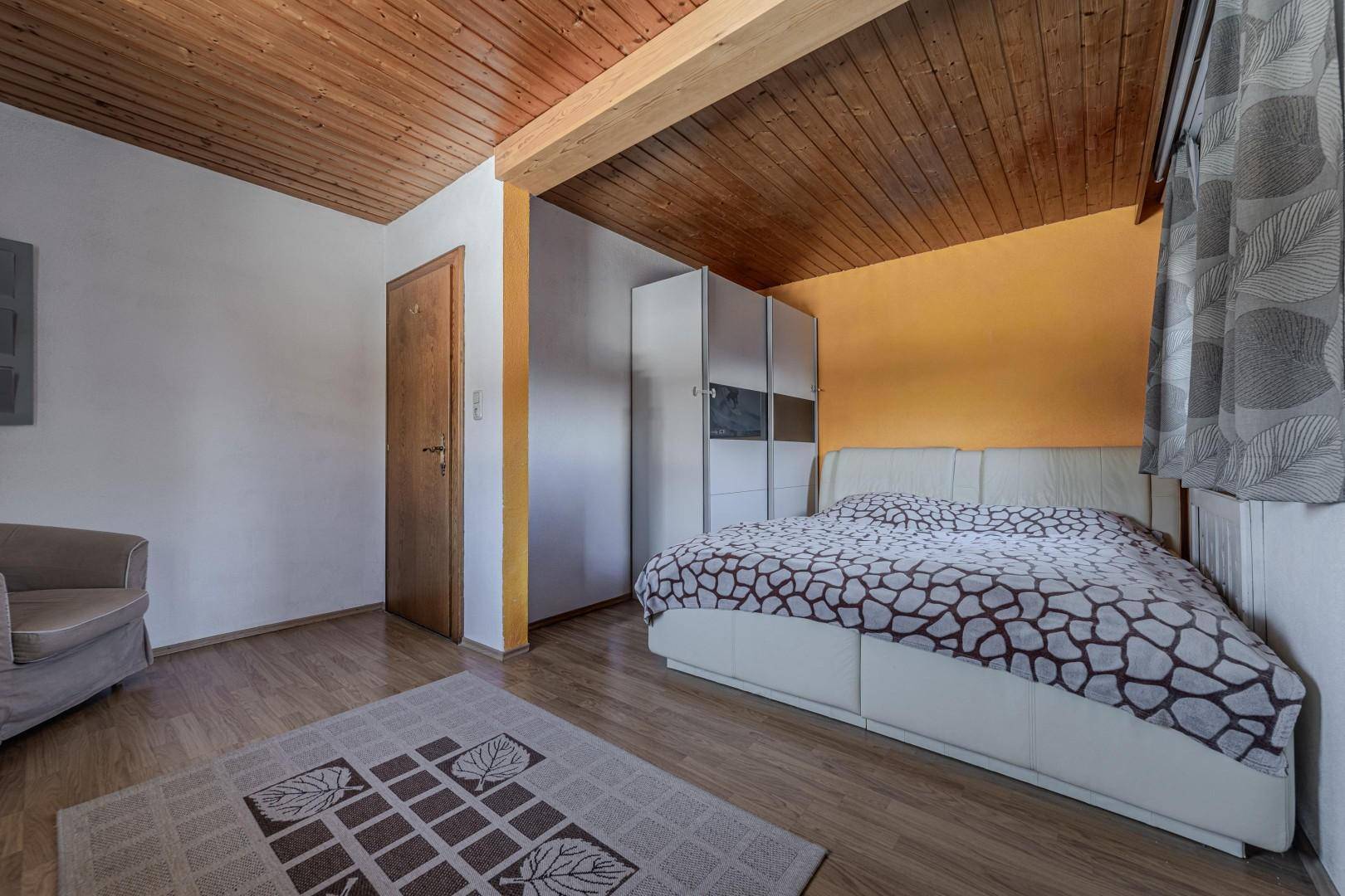 Geräumiges Schlafzimmer mit Holzbalkendecke, Einbauschrank und heller Einrichtung.