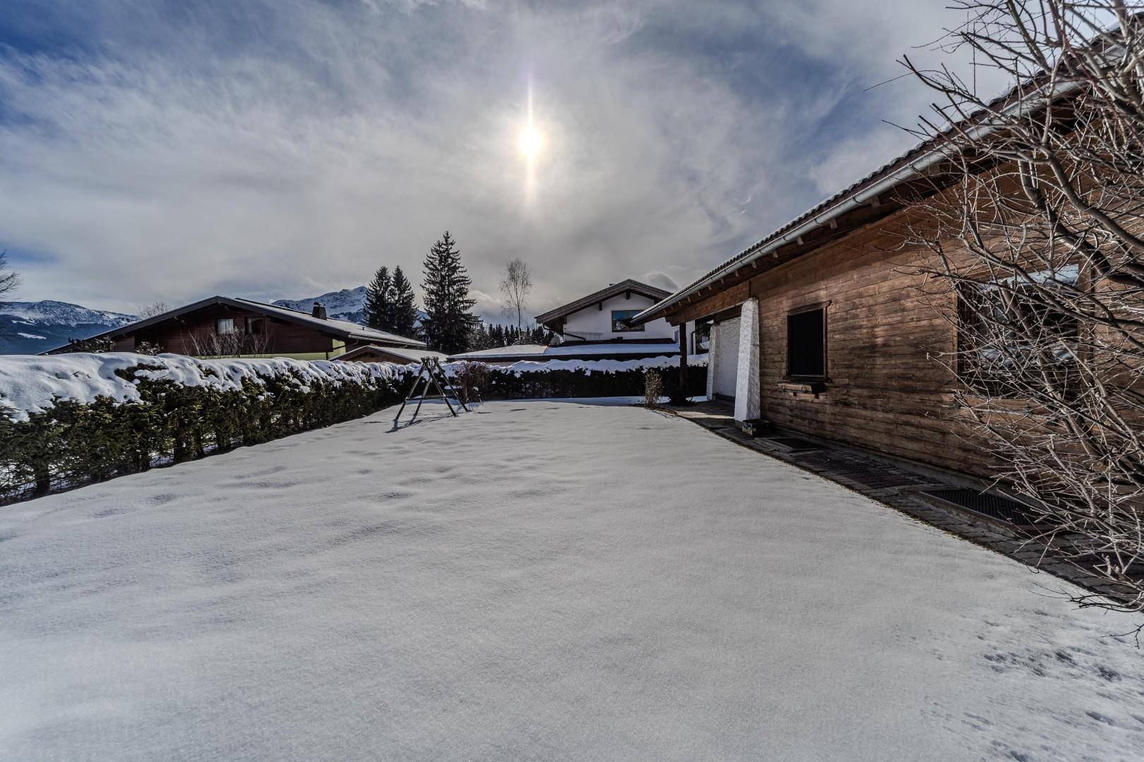 Sonniger, verschneiter Gartenbereich neben dem Haus mit Hecke und weitem Blick.